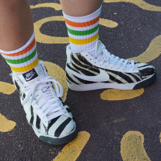 person wearing white mid calf socks with 3 orange, green, yellow stripes and zebra shoes 
